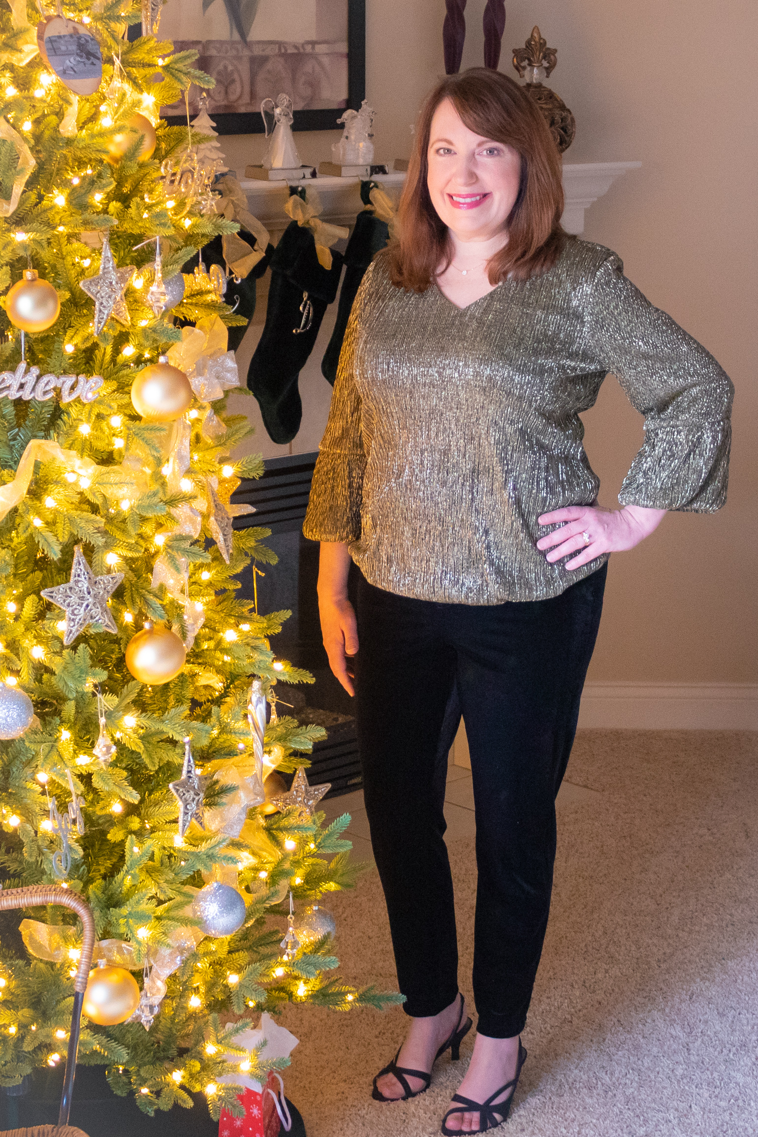 Dianna is standing by the Christmas tree dressed in metallic top and velvet pants.